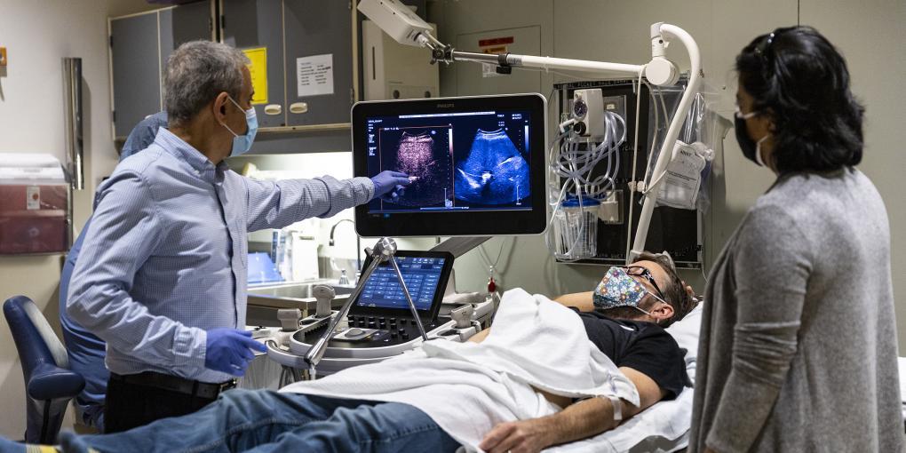 A man pointing at an ultrasound image in front of a patient